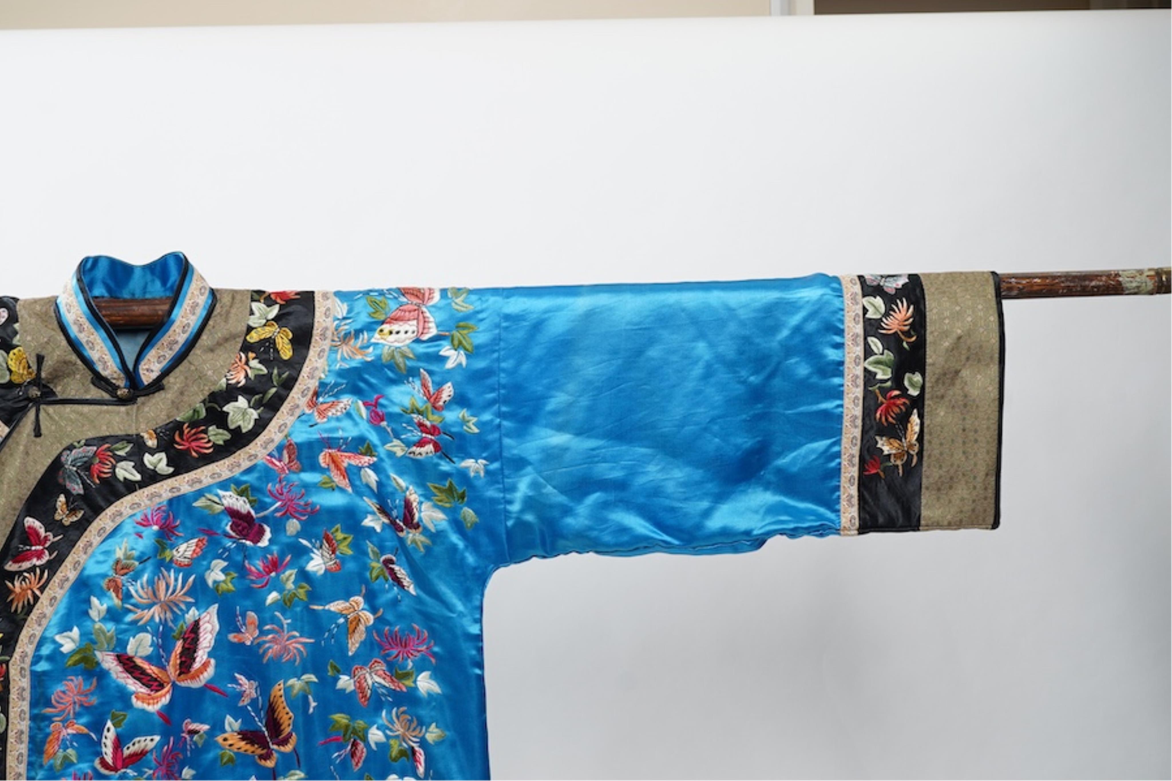 A mid 20th century Chinese turquoise silk jacket, with all over polychrome butterfly embroidery, similar embroidered sleeve bands, front and bottom edges on black silk, all bordered with gold brocade. The jacket blue sil